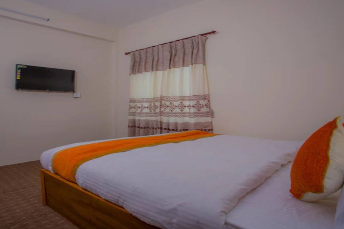 Ein Schlafzimmer mit einem Einzelbett, einem flachbildfernseher an der Wand und einem Fenster mit gemusterten Vorhängen.