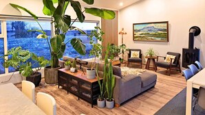 Una sala de estar moderna con un ventanal grande, un sofá, una mesa de comedor y varias plantas en macetas.