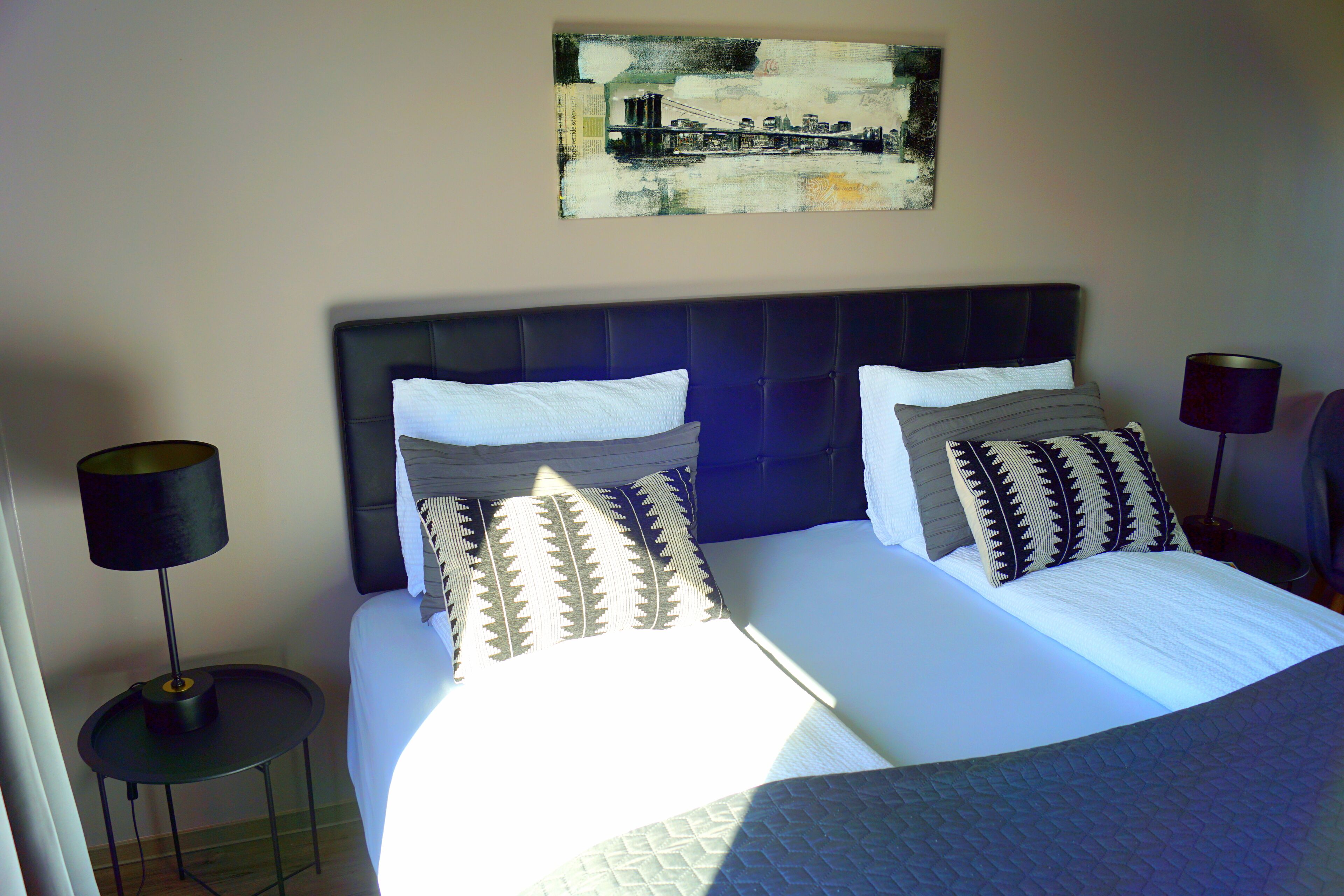 A double bed with a dark headboard, two bedside tables with lamps, and a painting on the wall.