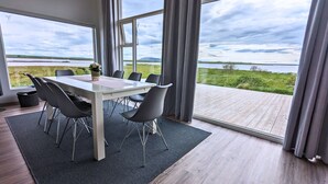 Un comedor moderno con una mesa y sillas, ventanas amplias y vistas a un lago y colinas.