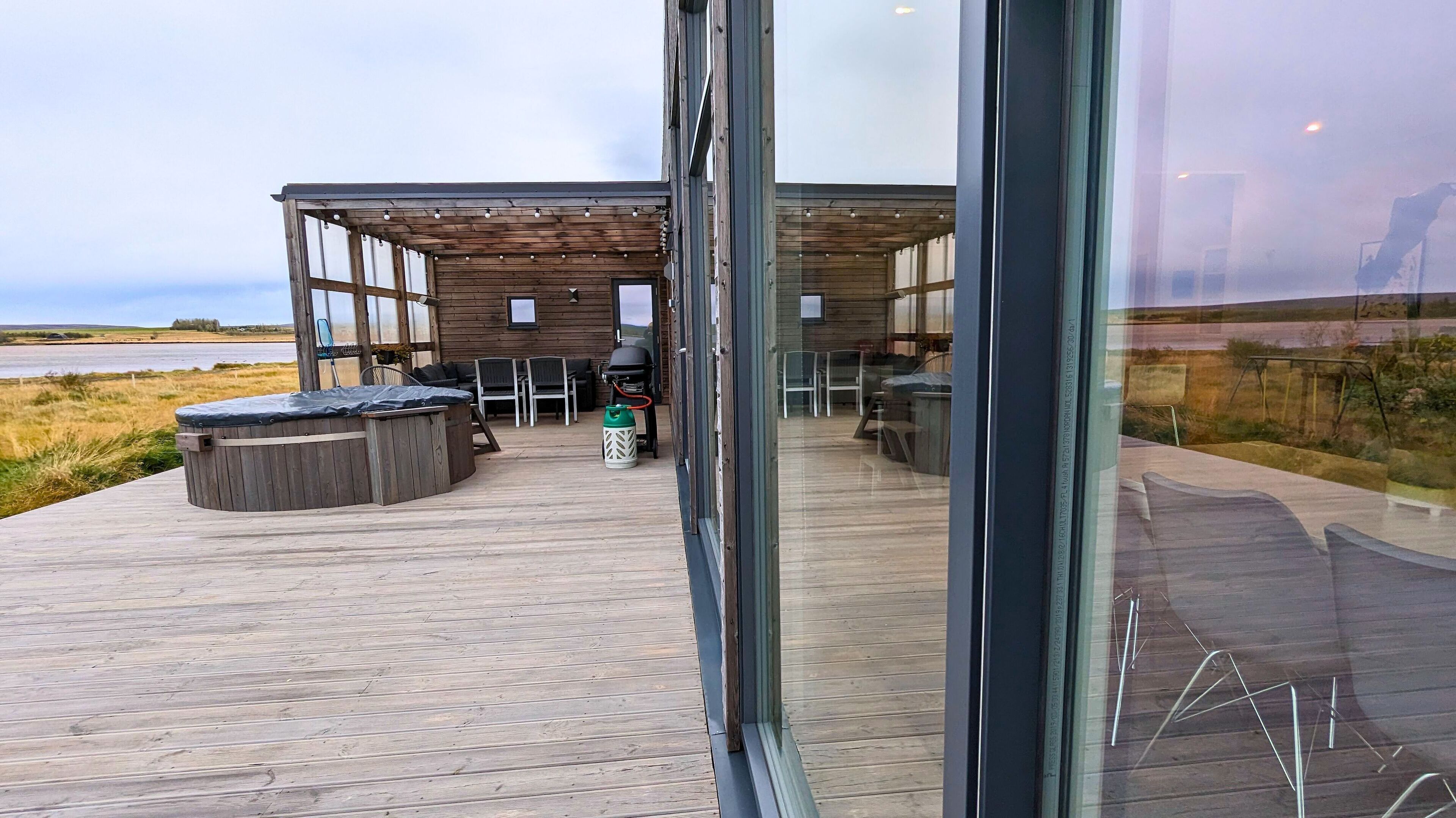 Une terrasse en bois avec un jacuzzi, un espace salon extérieur et un coin barbecue.