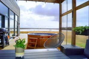 A covered outdoor area with a hot tub, seating, and a view of the beach. - Austurey Lakefront Villa (Bláskógabyggd)