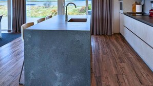 Una cocina moderna con una isla grande, suelo de madera y amplios ventanales que ofrecen vistas al exterior.