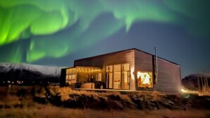 Un edificio moderno con ventanas grandes, ubicado en una colina cubierta de césped y vistas de la aurora boreal.