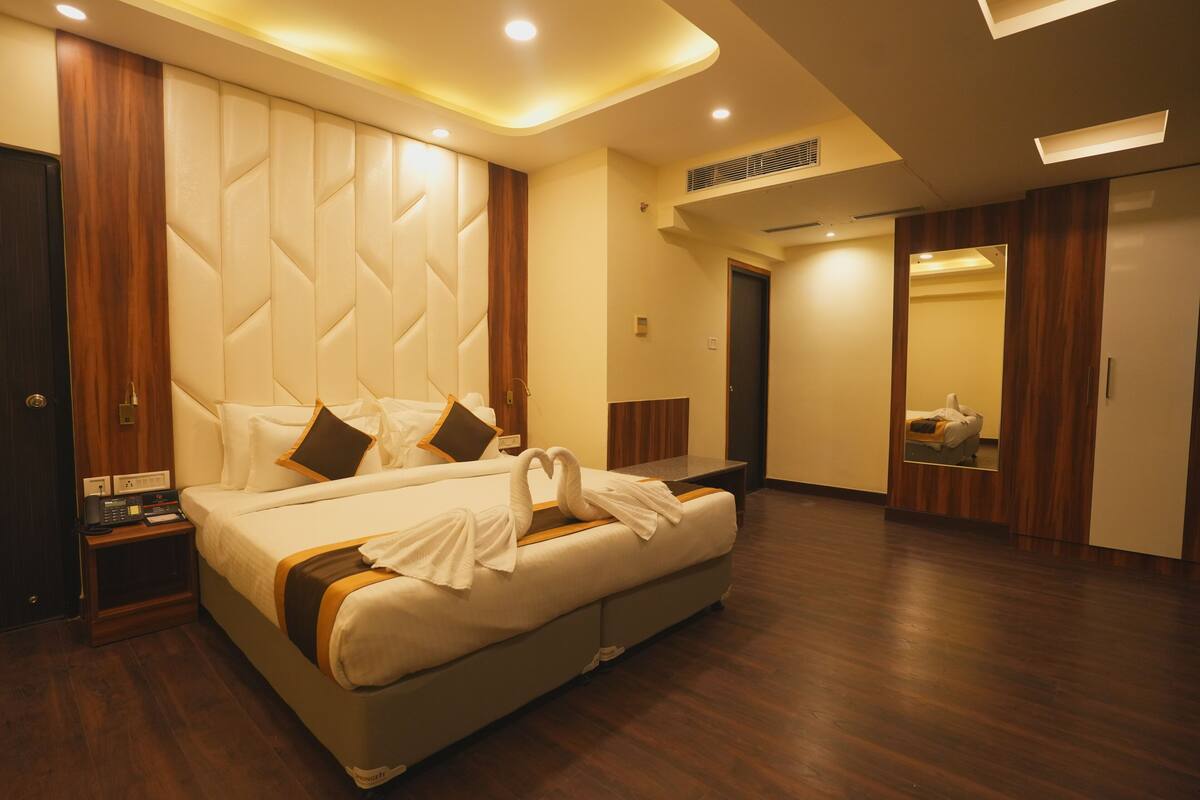 Una habitación de hotel moderna con una cama grande, suelo de madera y cabecero integrado.