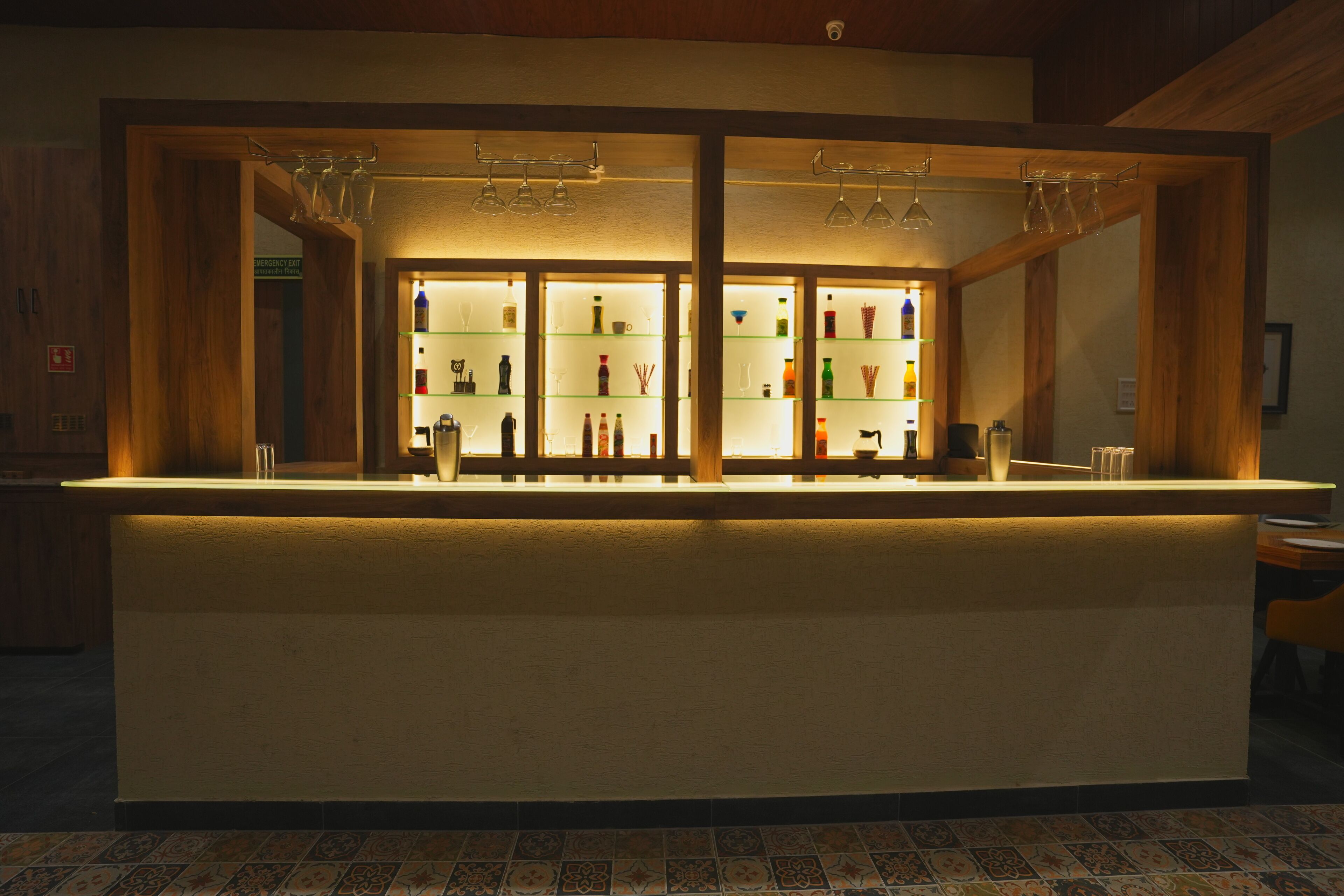 Zona de bar con estantes llenos de botellas y vasos, una barra y techo de madera.