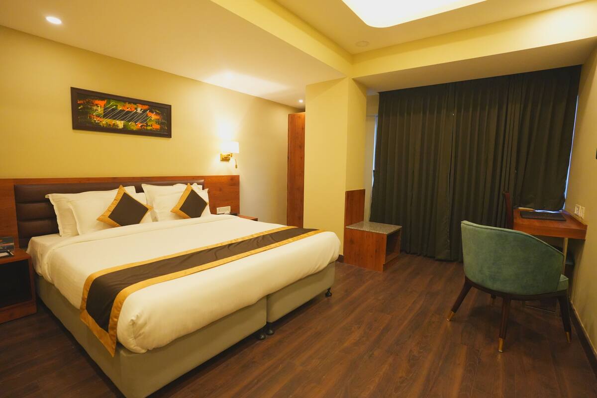 Habitación de hotel con una cama grande, un escritorio, una silla, un cuadro en la pared y una cortina.