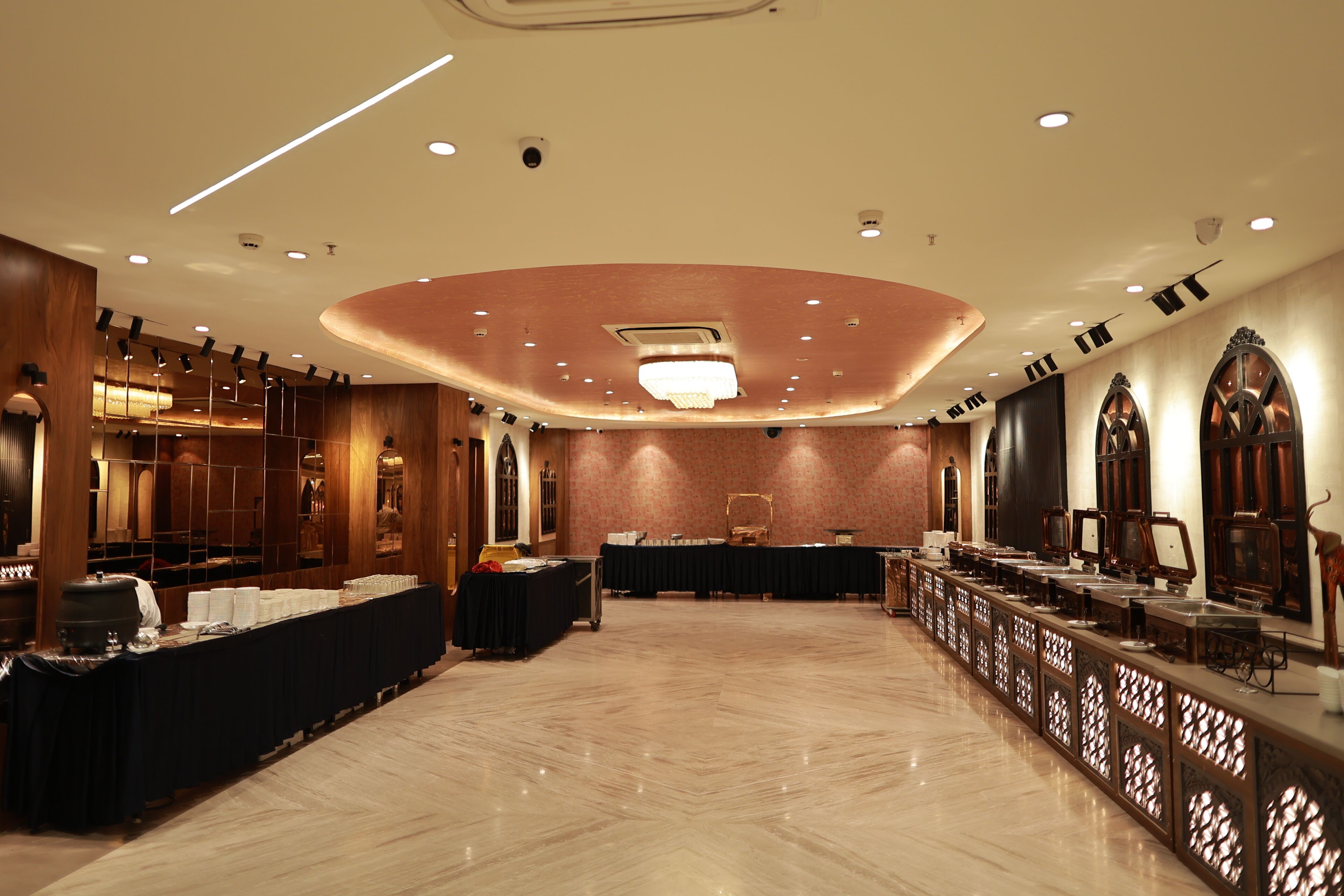 A spacious banquet hall with a polished marble floor, a long buffet table, and a high ceiling with recessed lighting.