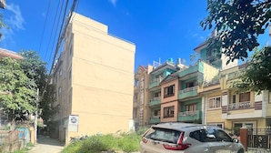 A residential area with a beige building, a parked car, and a narrow pathway. - Hotel Down to Earth  (Kathmandu)