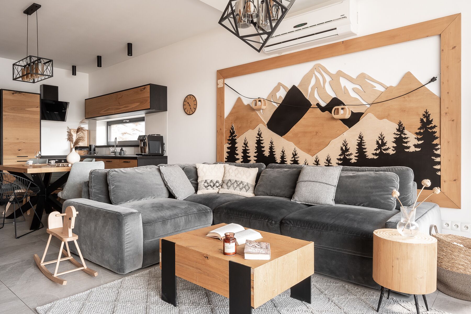 Un salon moderne avec un canapé d’angle gris, une table basse en bois et une grande fresque murale représentant des montagnes.