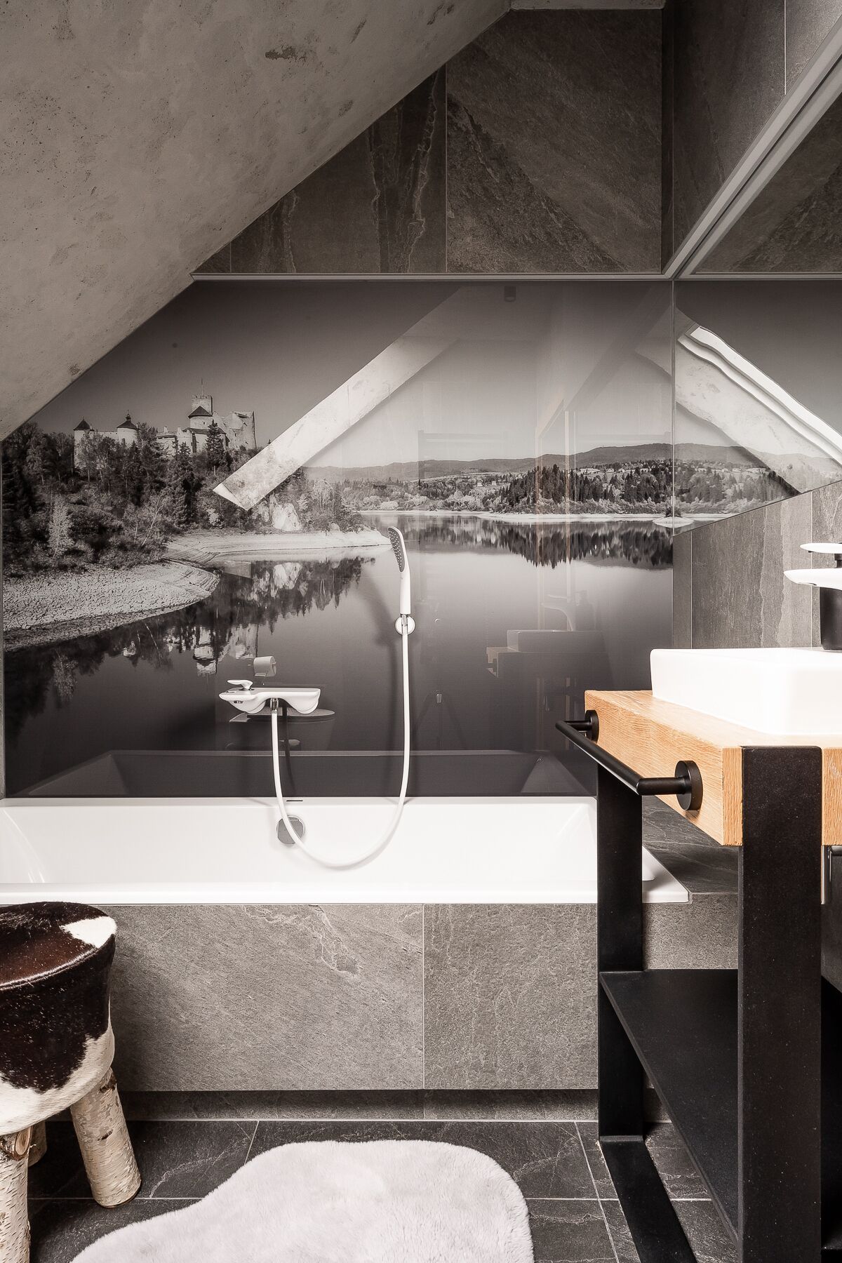 Un baño moderno con una bañera grande, un tocador de madera y vistas a un lago y montañas a través de un ventanal amplio.