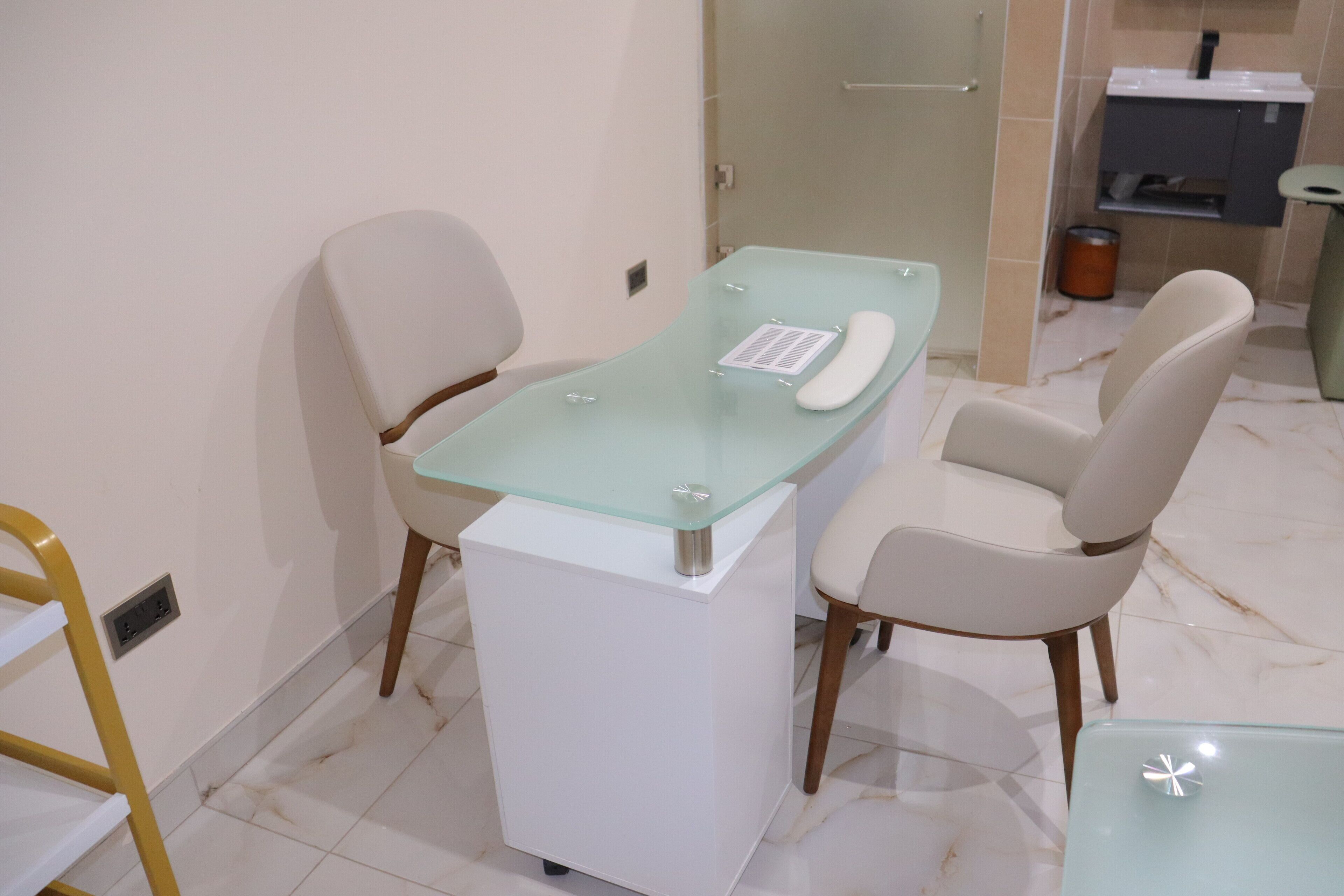 A modern office with a glass desk, two chairs, a telephone, and a trash bin.