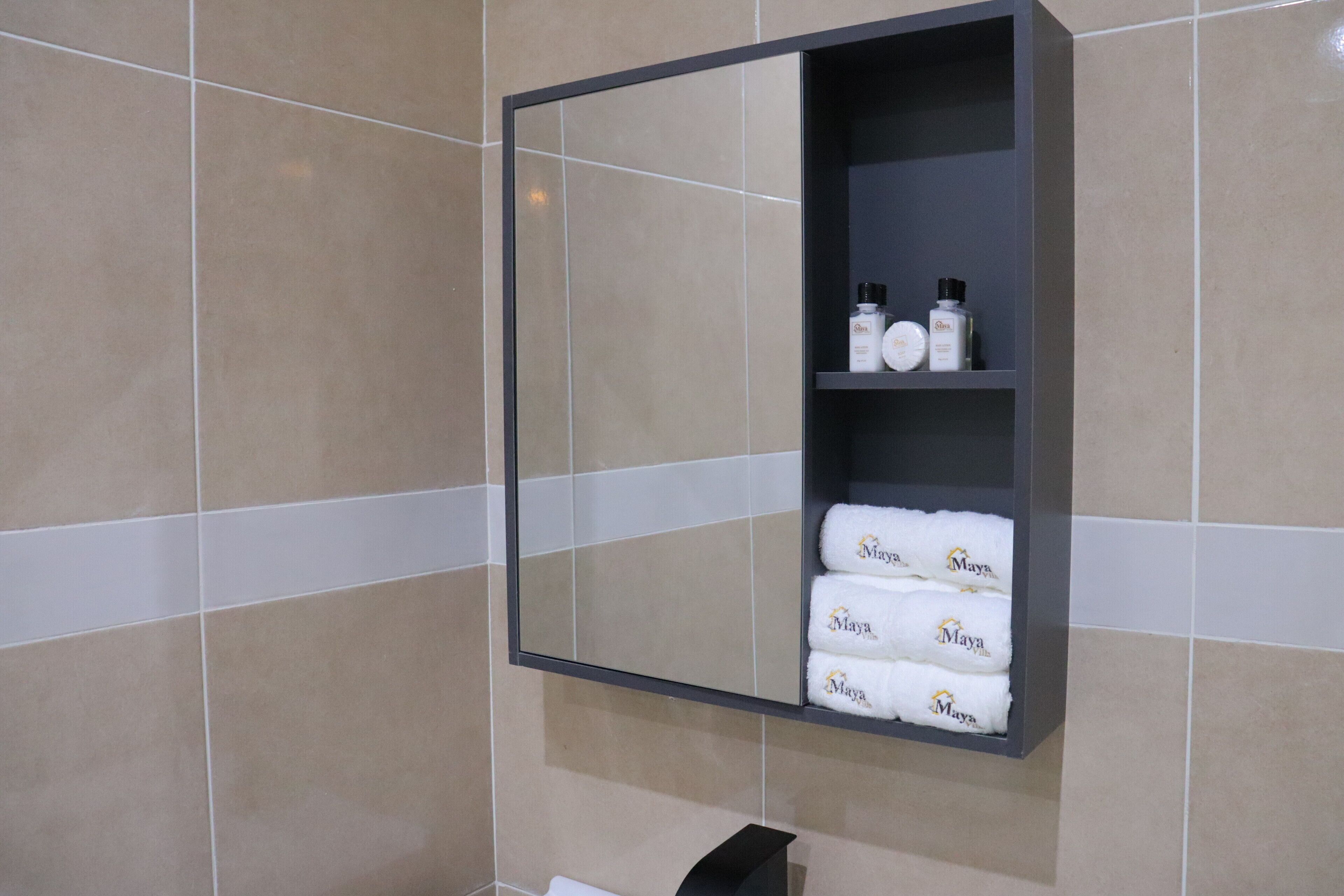 Un baño con pared de azulejos, un espejo y un estante con artículos de aseo y toallas.