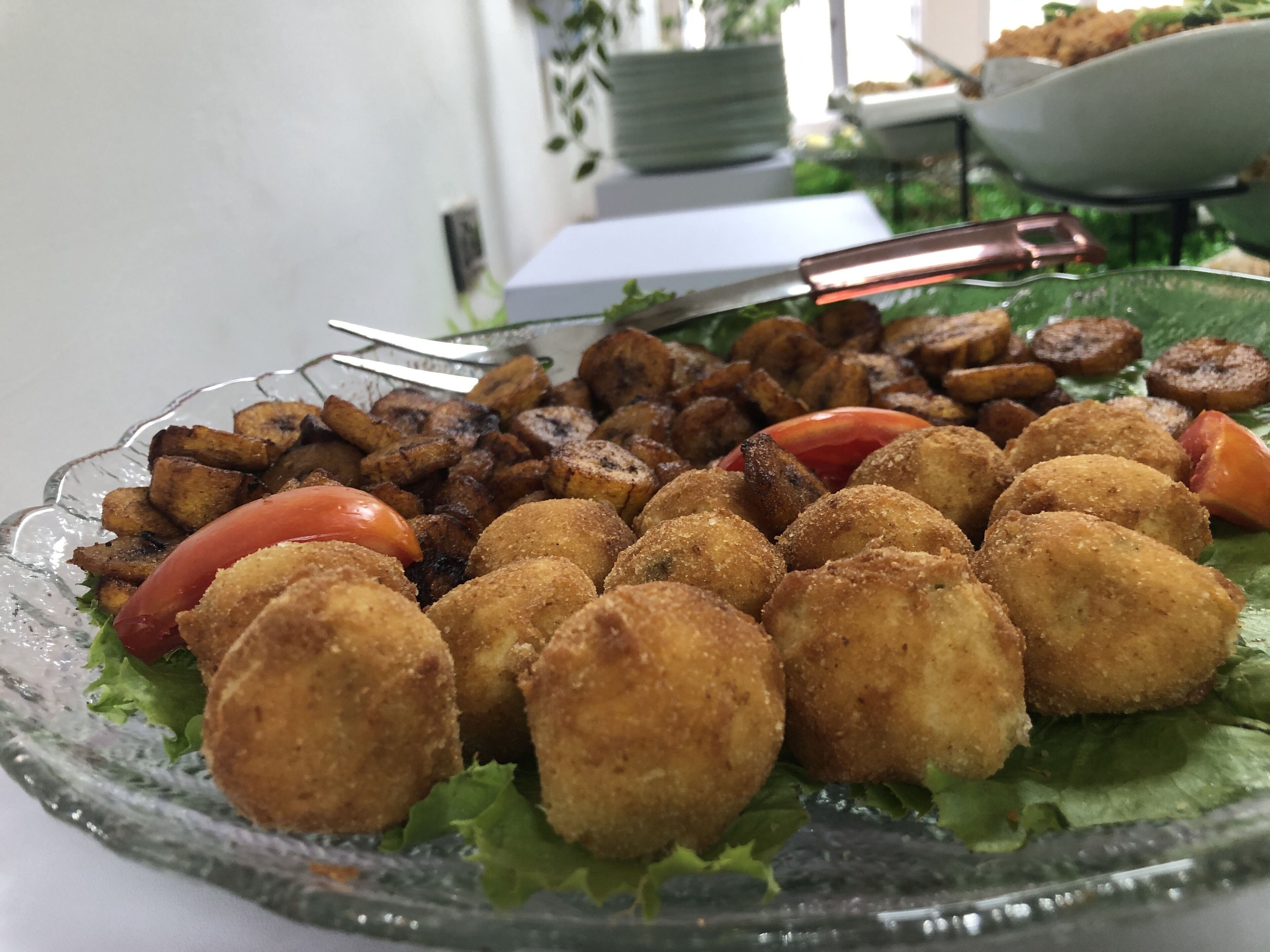 A glass plate with fried food items, including croquettes and fried potatoes, on a bed of lettuce.