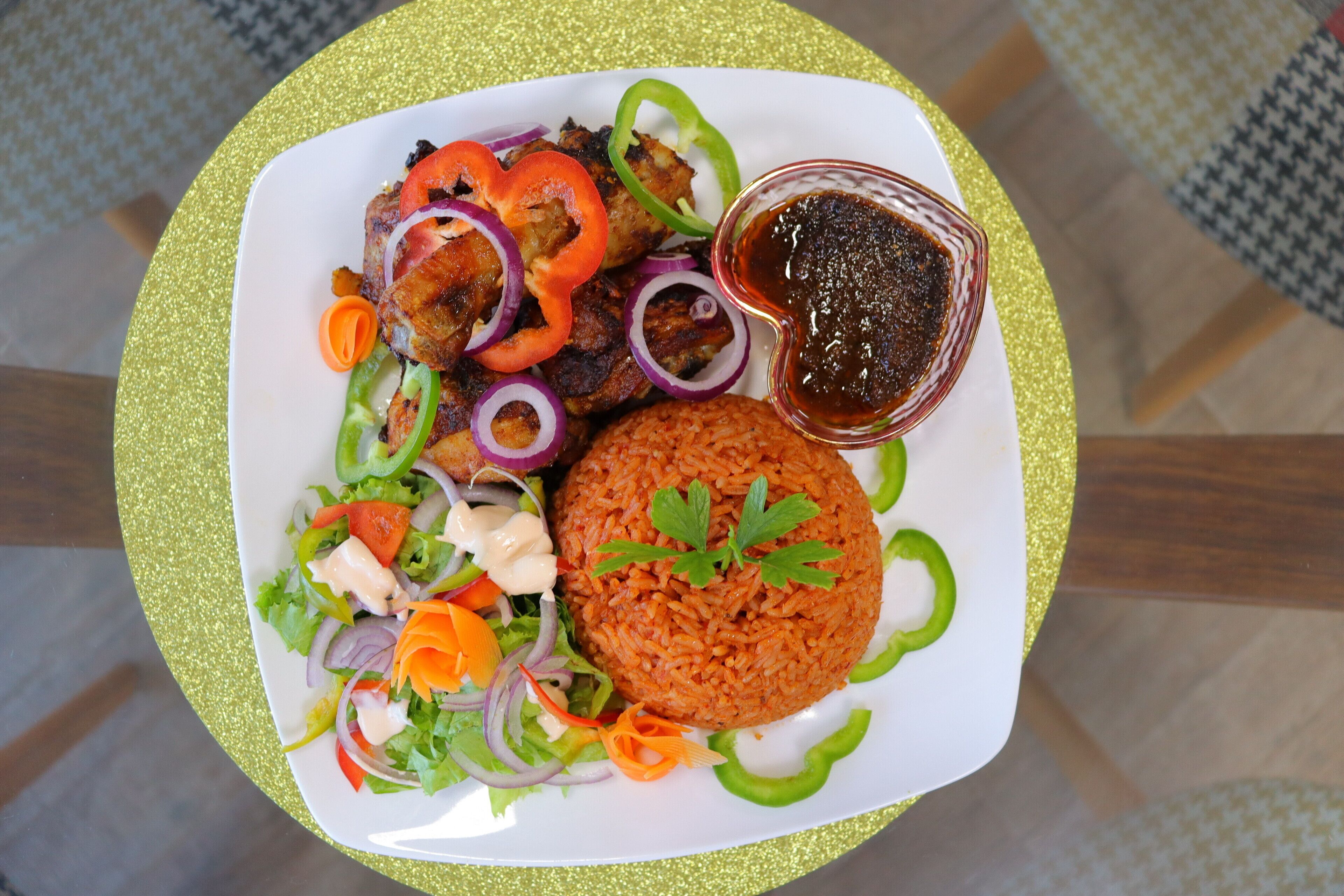 A plate with rice, grilled meat, and vegetables, served on a glittery gold plate.