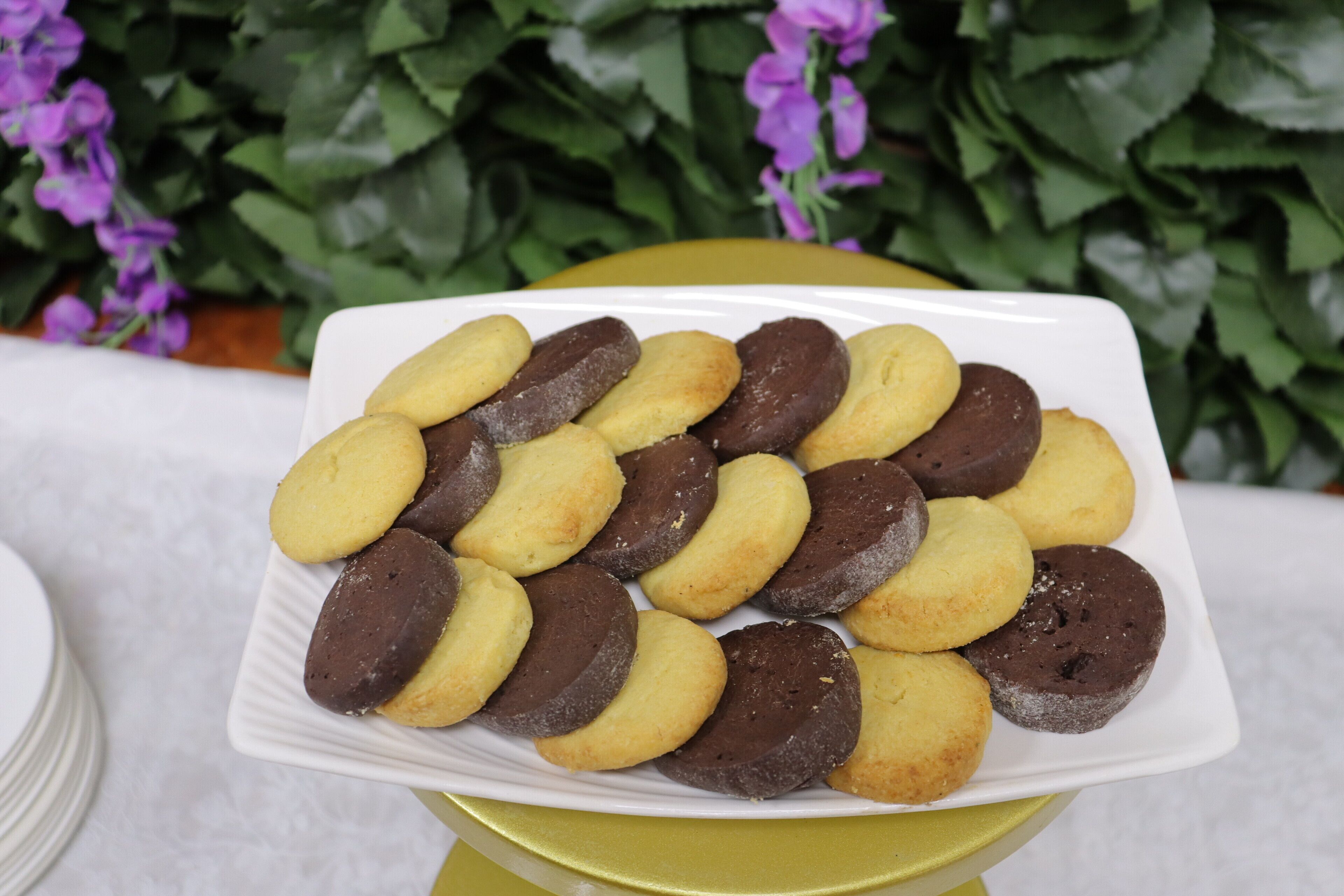 A white plate with assorted cookies on a yellow table.