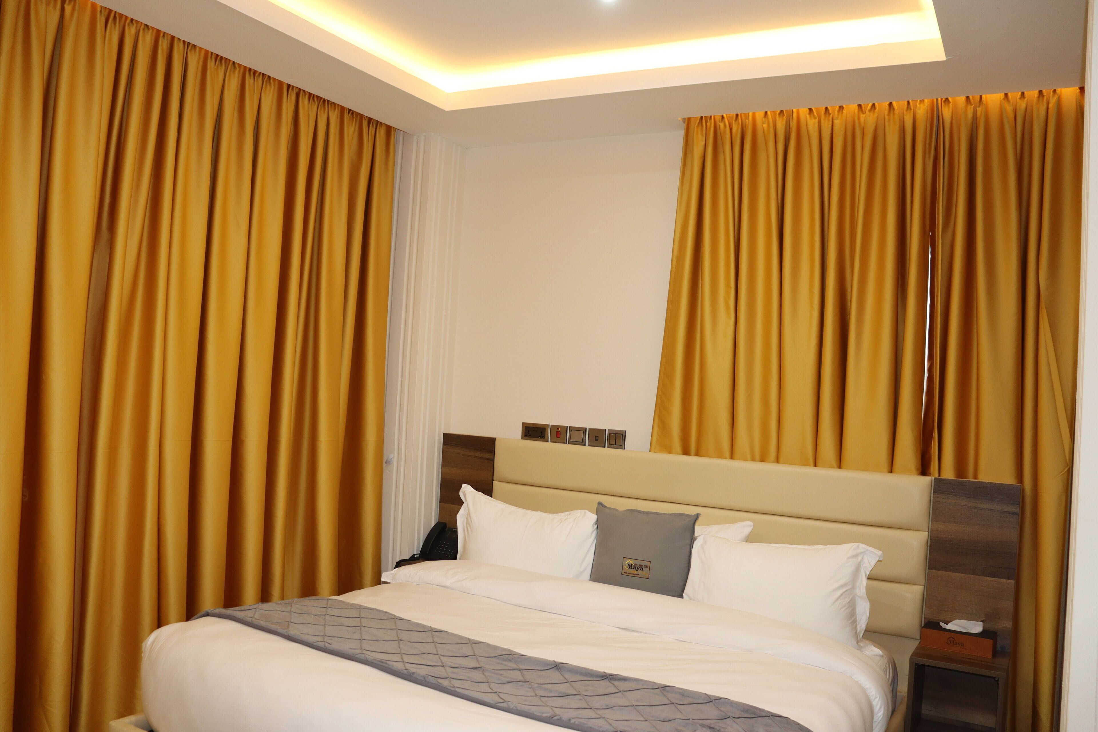 A hotel room with a large bed, a headboard with a clock, and curtains on the windows.