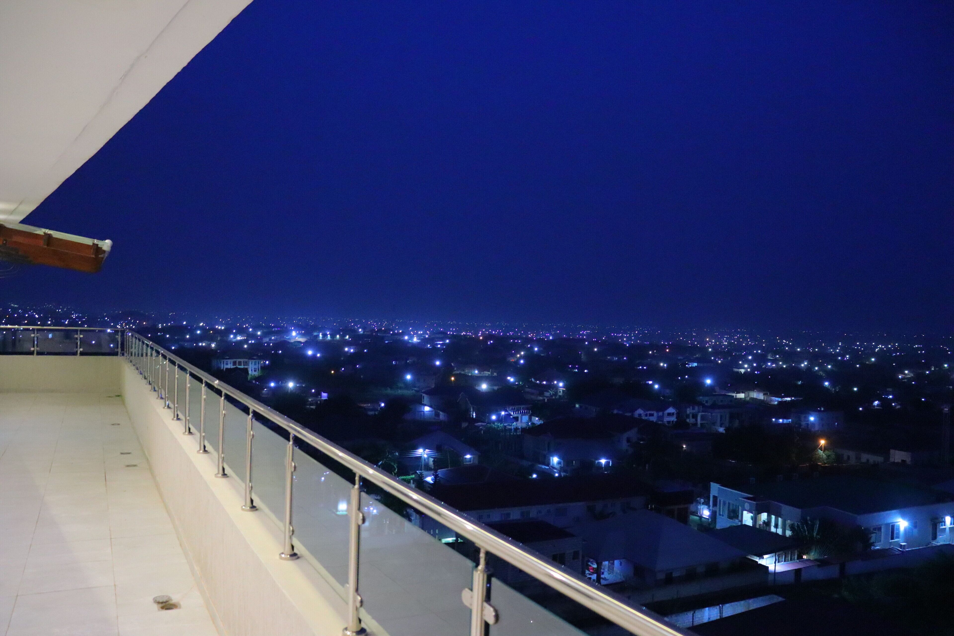 A night view from a balcony overlooking a cityscape with illuminated buildings.