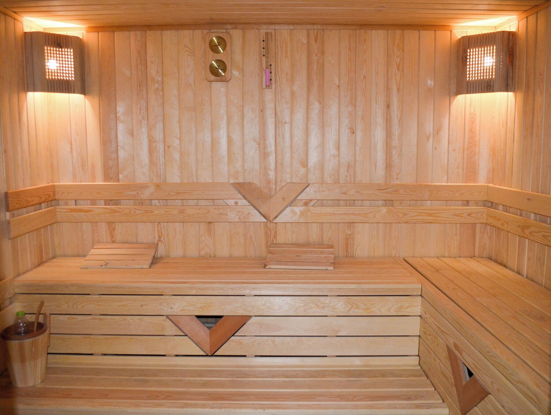 Una sauna in legno con panche, un elemento riscaldante centrale e due luci a parete.