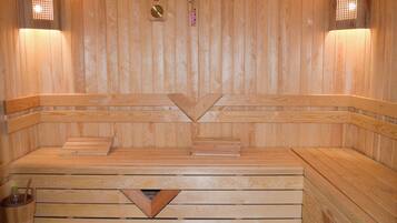 Una sauna in legno con panche, un elemento riscaldante centrale e due luci a parete.