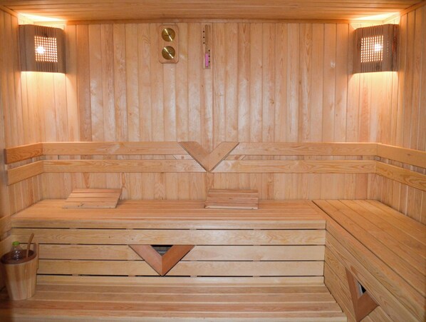 Una sauna de madera con bancos, un calentador central y dos luces fijadas a la pared.
