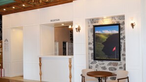 Un área de recepción con mostrador, dos sillas, una mesa y un cuadro con un paisaje en la pared.