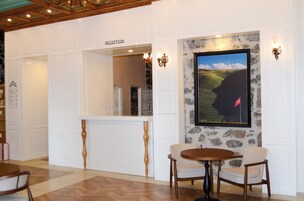Un área de recepción con mostrador, dos sillas, una mesa y un cuadro con un paisaje en la pared.
