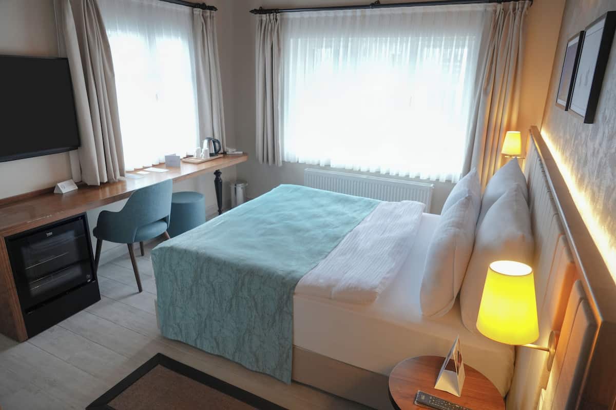 Habitación de hotel con cama, escritorio, silla, televisor y lámpara.