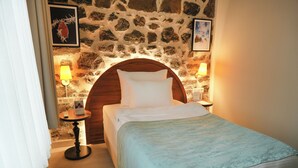Un dormitorio acogedor con pared de piedra, cabecera de madera, cama con ropa blanca y dos lámparas de noche.