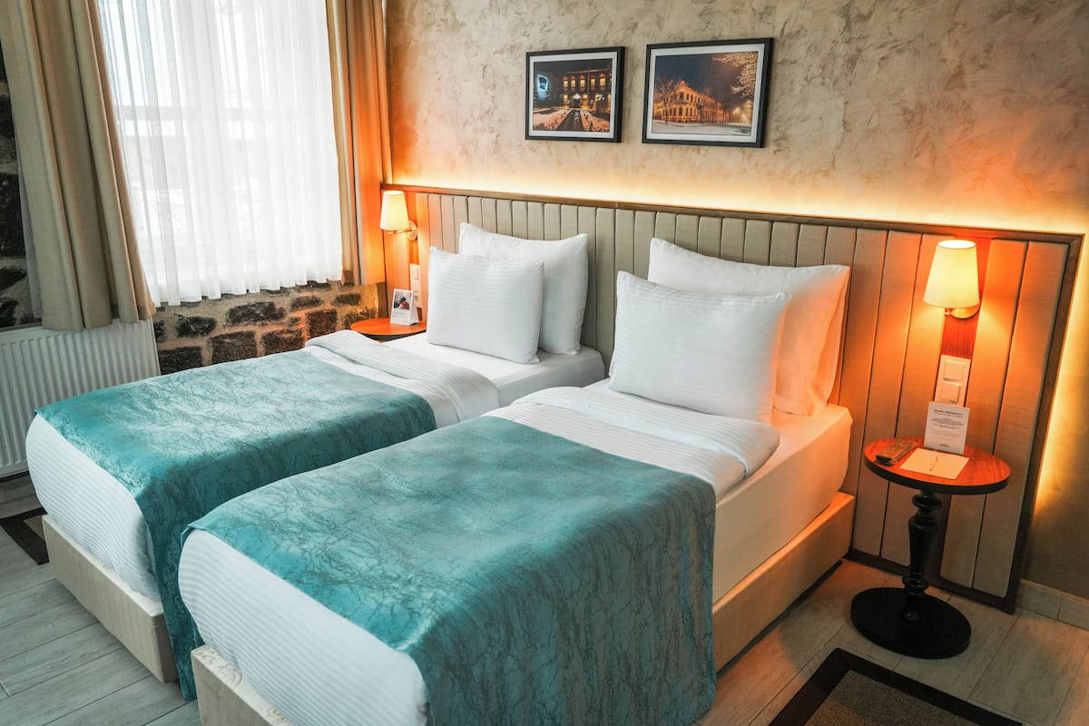 Habitación de hotel con dos camas, una pared de piedra, un radiador y dos cuadros enmarcados.