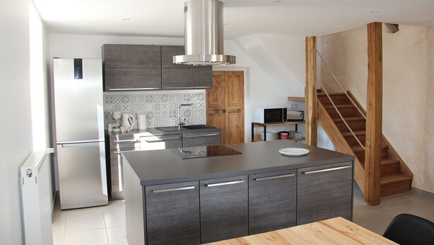 Een moderne keuken met een centraal eiland, inbouwapparatuur en een houten trap.