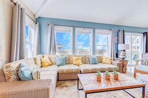 A living room with a sectional sofa, a herringbone coffee table, and a view of a balcony with a railing. - Oceanfront Cottage w/ Private Pool, Hot Tub, and Nearby Boardwalk to Beach (Avon)