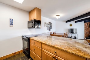Kitchen with a large island, sink, and dining area, featuring a brick wall and exposed beams.