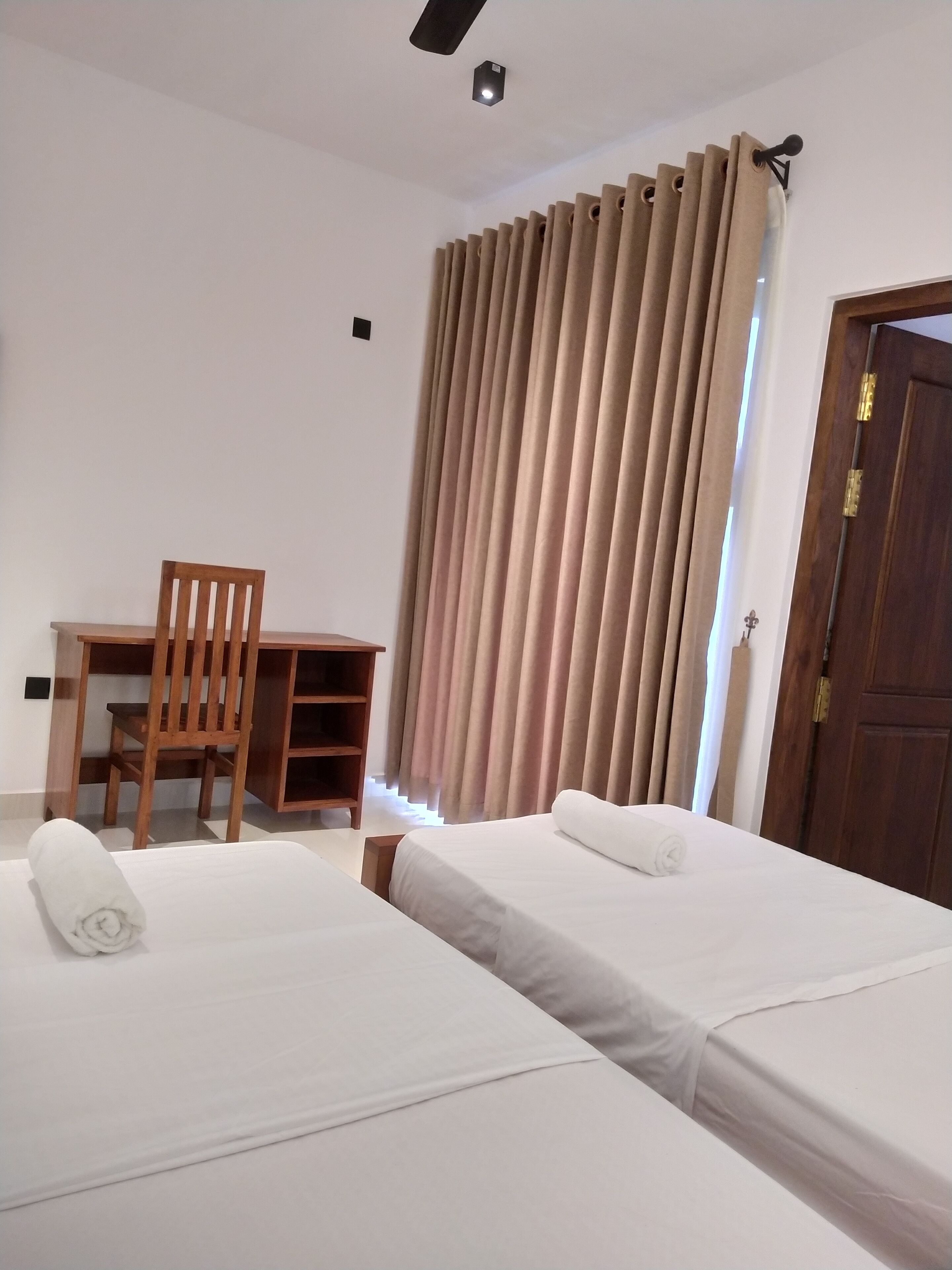 A hotel room with two beds, a wooden desk, and a chair.