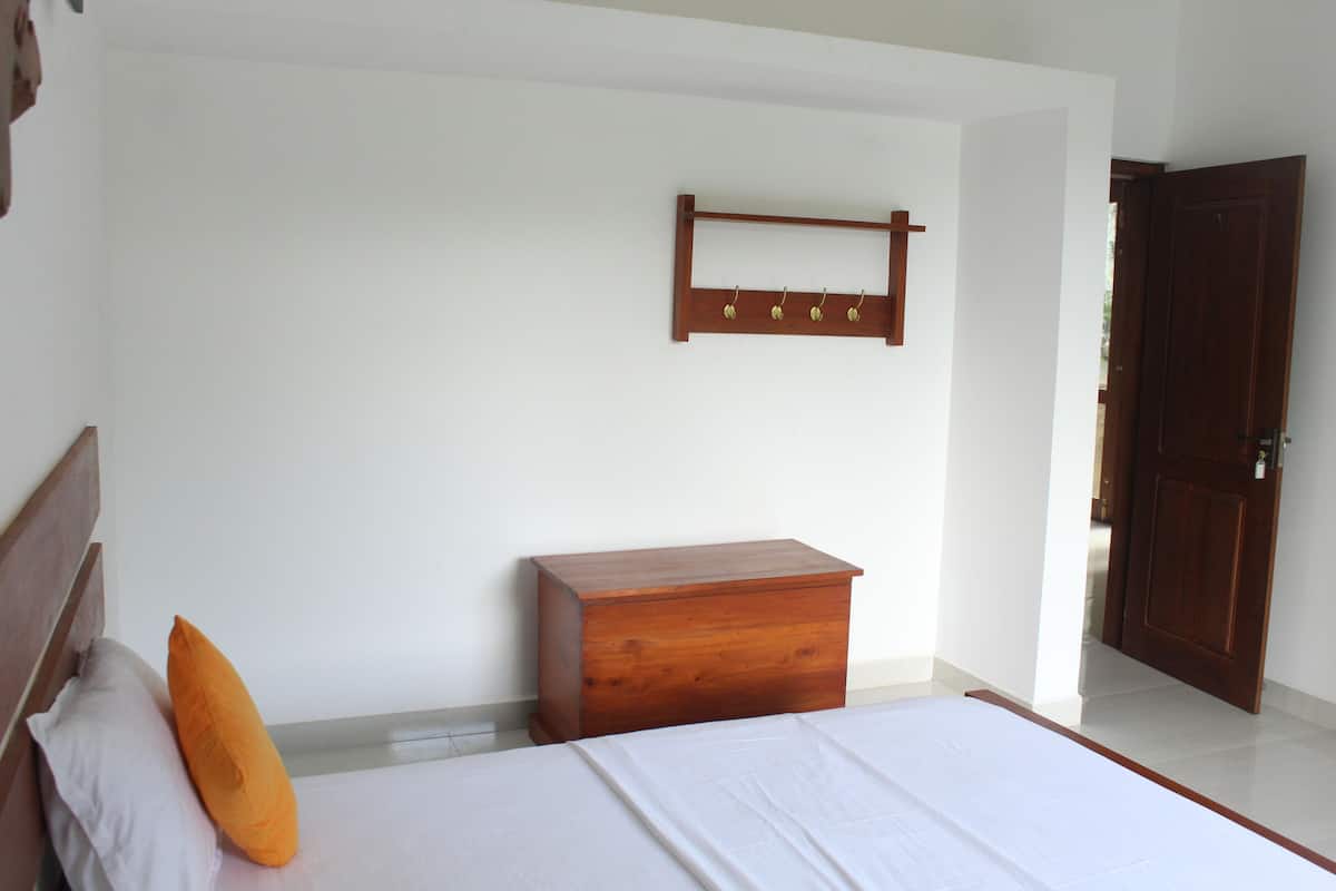 A bedroom with a bed, a wooden nightstand, a wall-mounted coat rack, and a door.