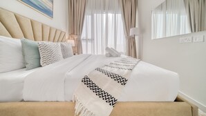 Een netjes opgemaakt bed met een beige hoofdbord, witte beddengoed en een gestreept plaid.
