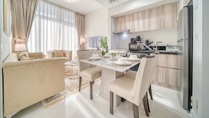 Een moderne woonkamer met een bank, eettafel en stoelen. Er is een keuken met kasten en apparatuur.