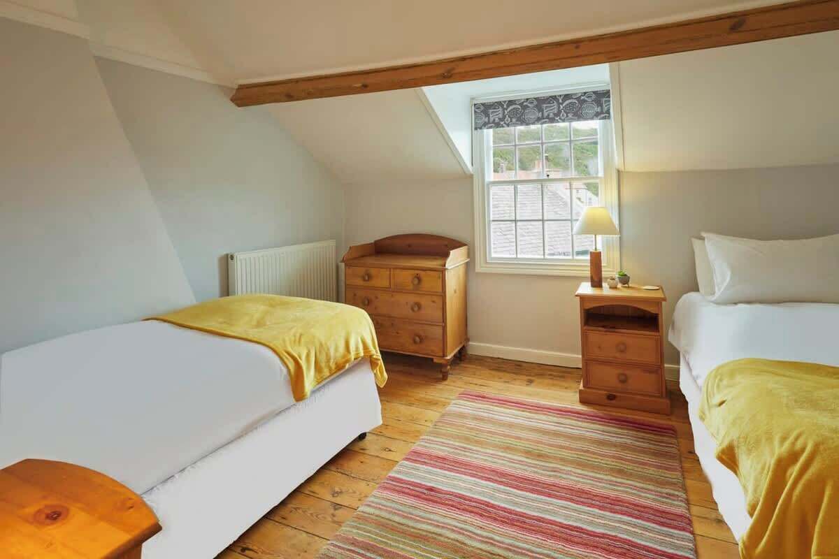 A bedroom with two beds, a window, a radiator, and a wooden dresser.