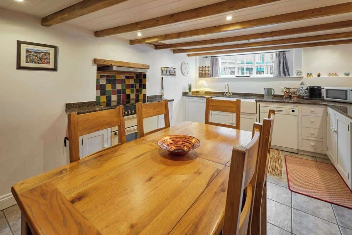 A dining area with a wooden table and chairs, a colorful backsplash, and a window with curtains.