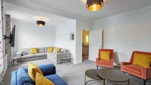 Una sala de estar moderna con un sofá gris, un sofá azul y dos sillones rojos con cojines amarillos. Hay una pequeña mesa en el centro.