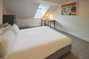 Ett sovrum med en stor säng, ett skrivbord, en stol och ett element.