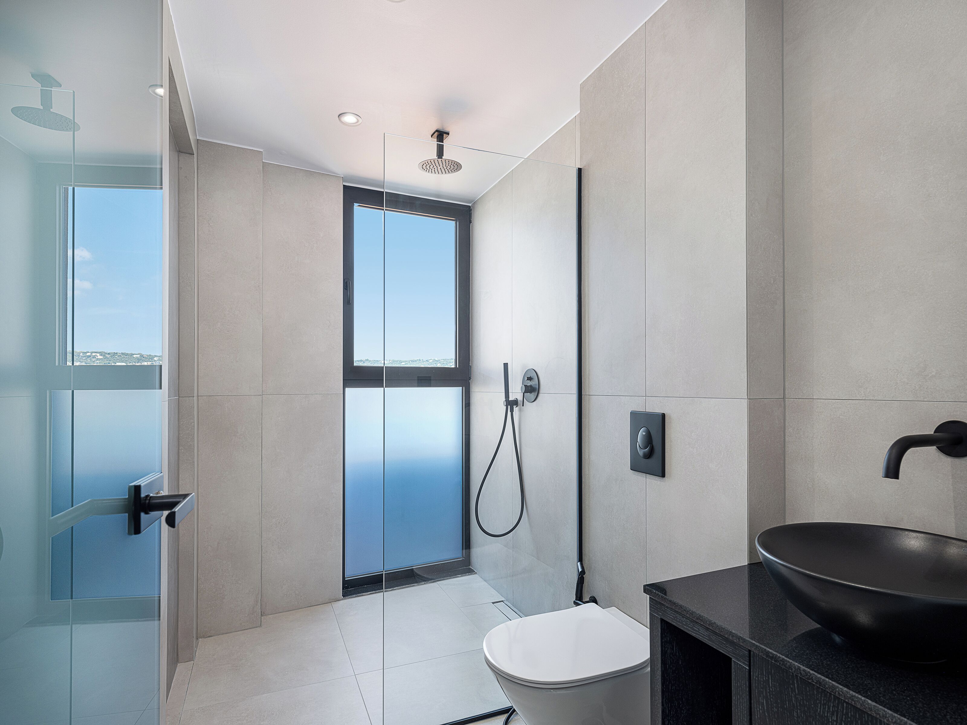 A modern bathroom with a glass shower enclosure, a toilet, and a large black basin.