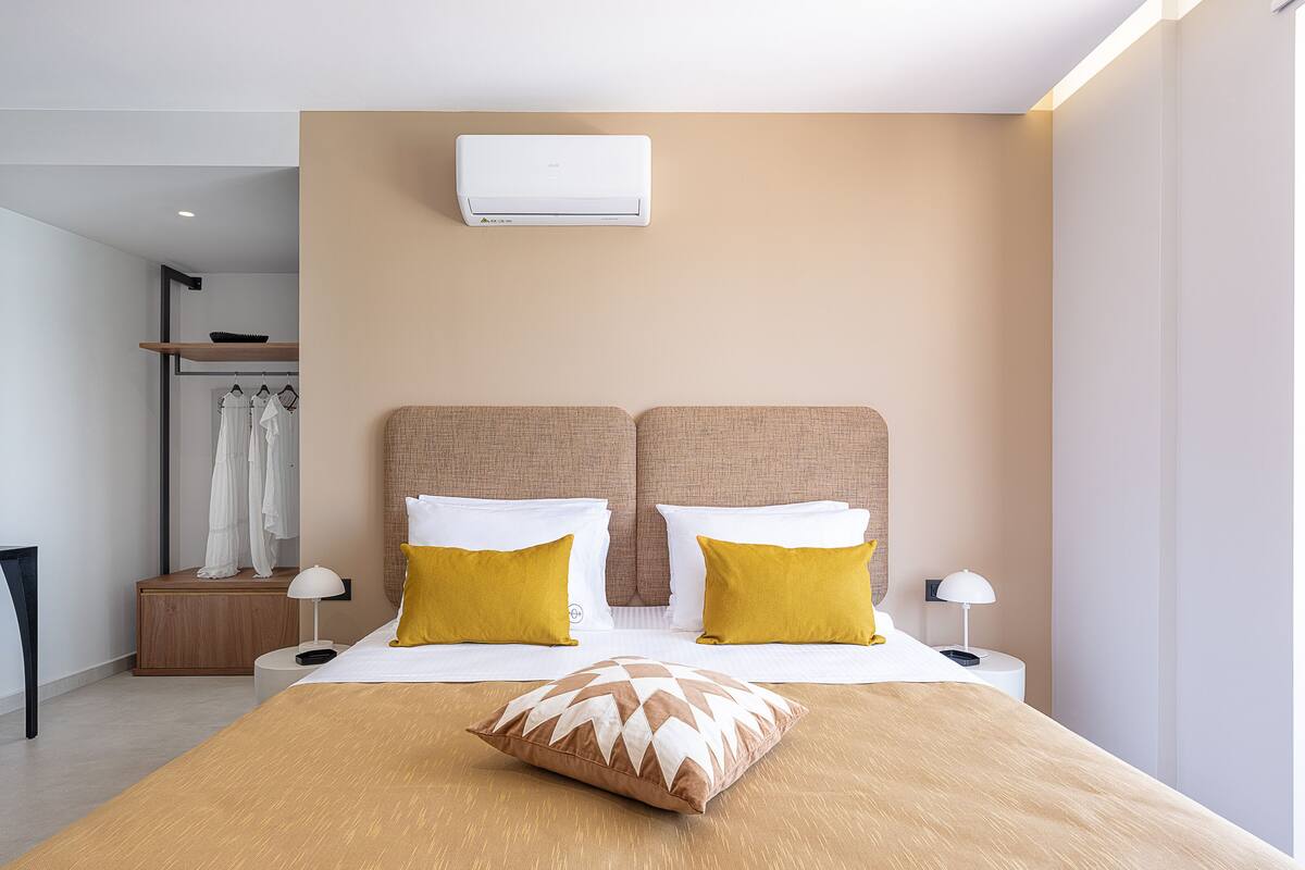 Quarto de hotel moderno com uma cama grande, duas mesas de cabeceira, um guarda-roupa e um aparelho de ar condicionado.
