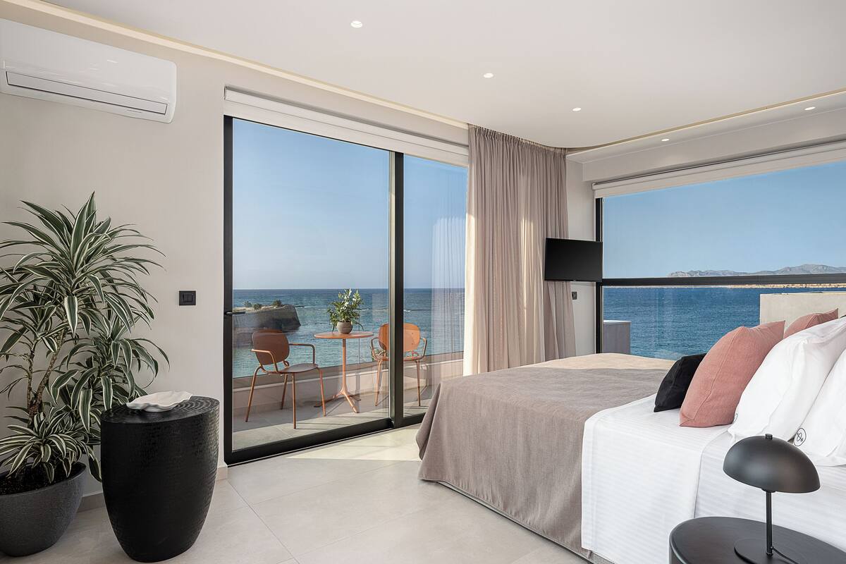Quarto de hotel moderno com uma cama grande, televisão e varanda com vista para o mar.
