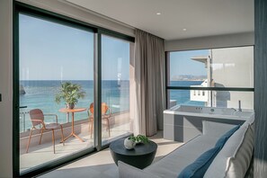 Een modern balkon met uitzicht op zee, een zithoek met een tafel en stoelen, en een klein keukenhoekje.