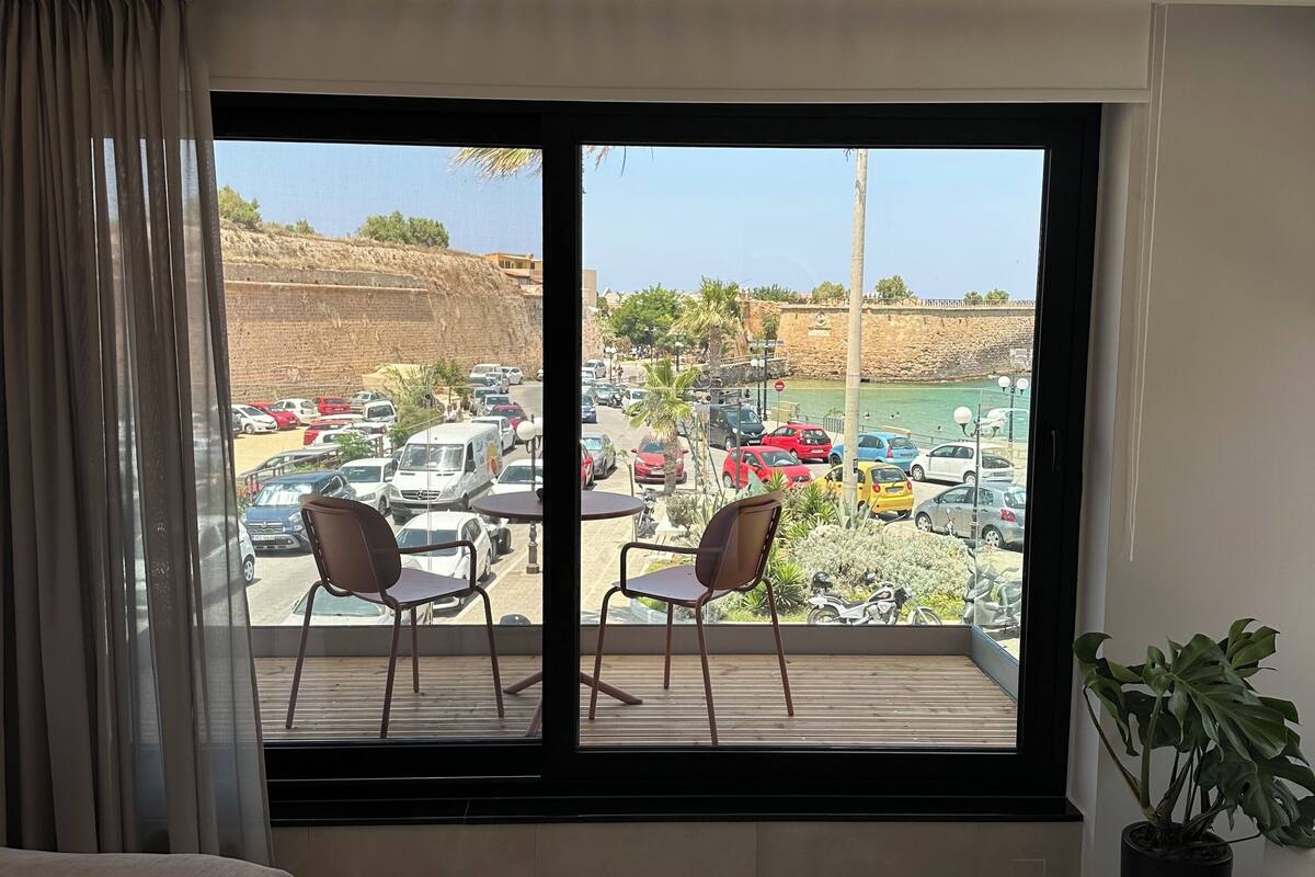 Quarto de hotel com uma janela ampla de frente para um estacionamento e uma praia.