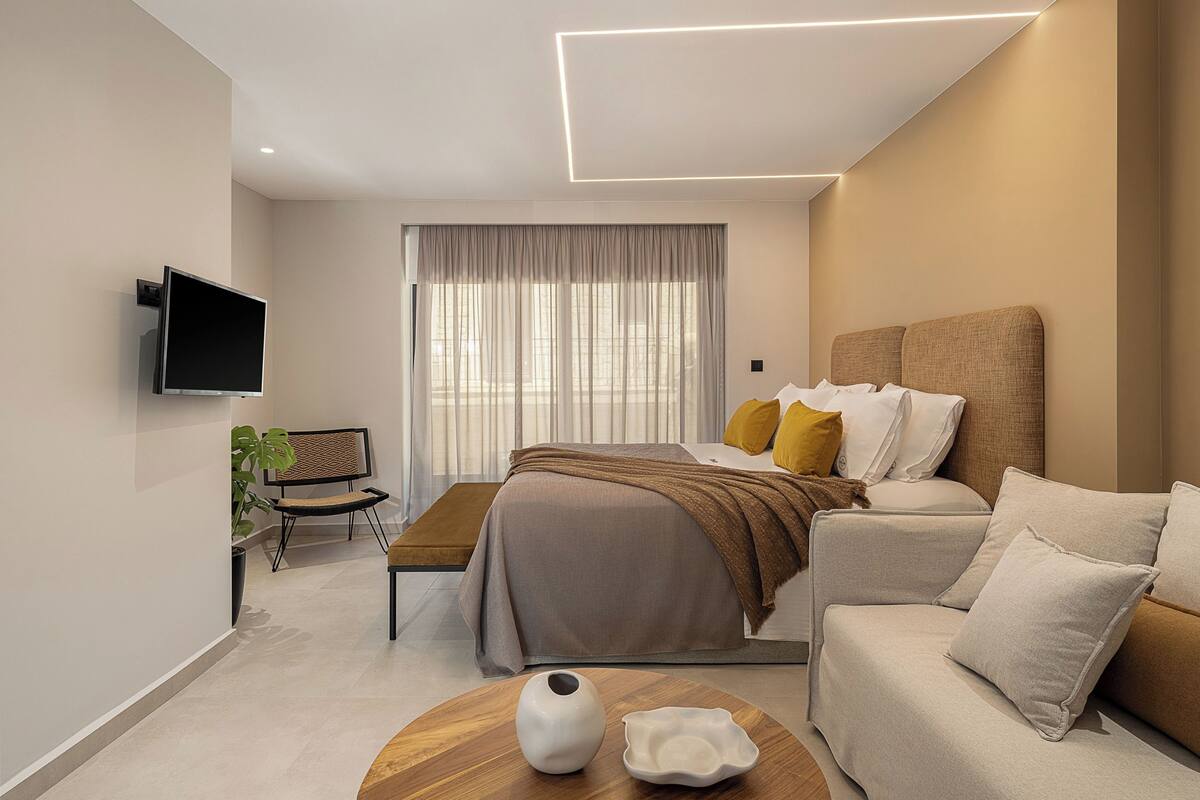 Quarto de hotel moderno com cama, sofá, televisão e uma pequena mesa com um vaso.