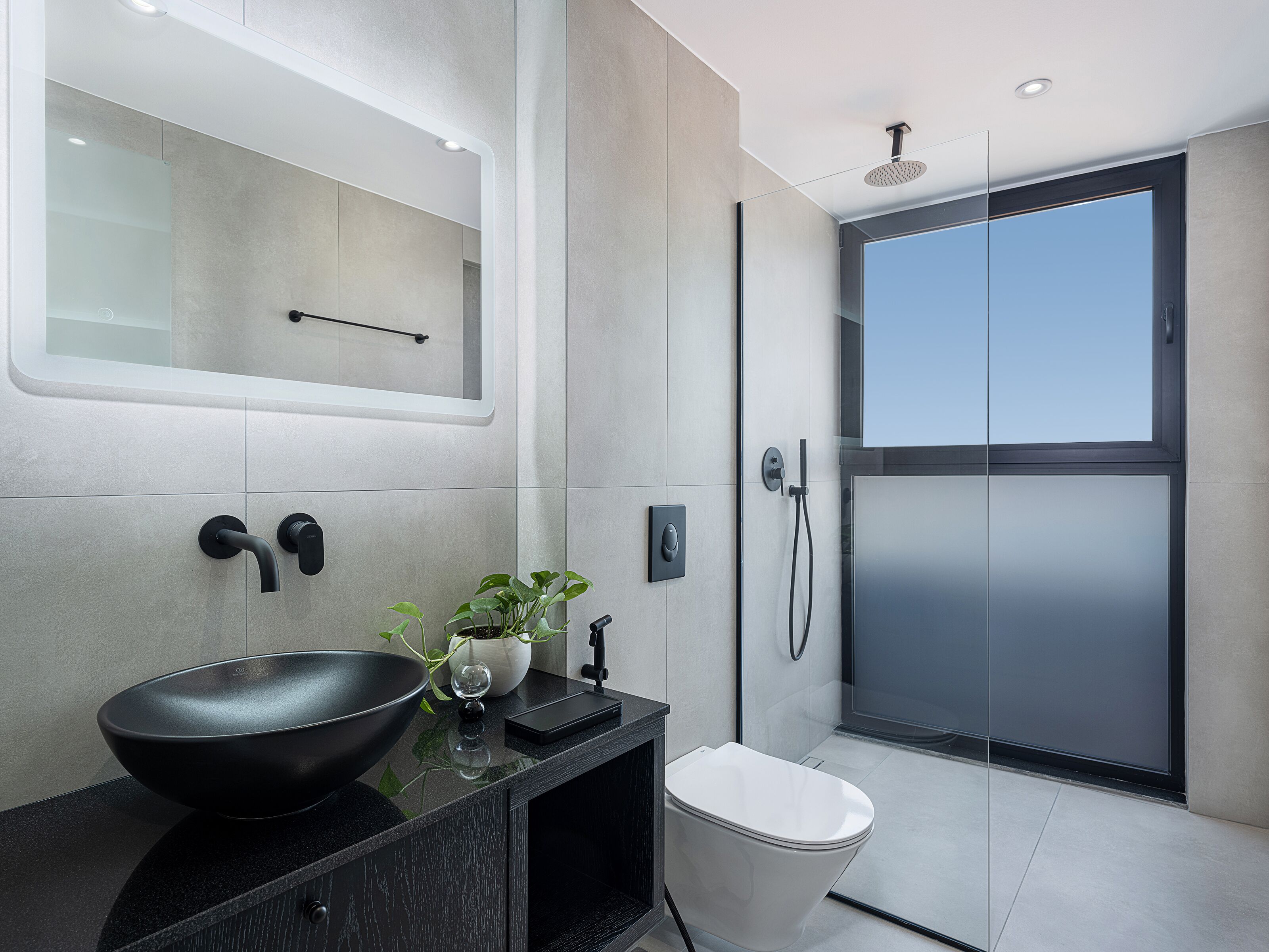 A modern bathroom with a black sink, a mirror, a shower, and a toilet.