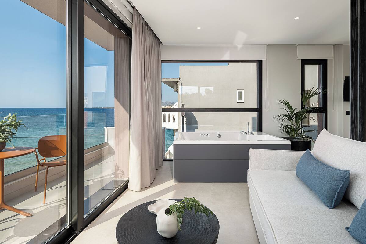 Uma varanda moderna com vista para o mar, um sofá, uma mesa pequena e uma planta.