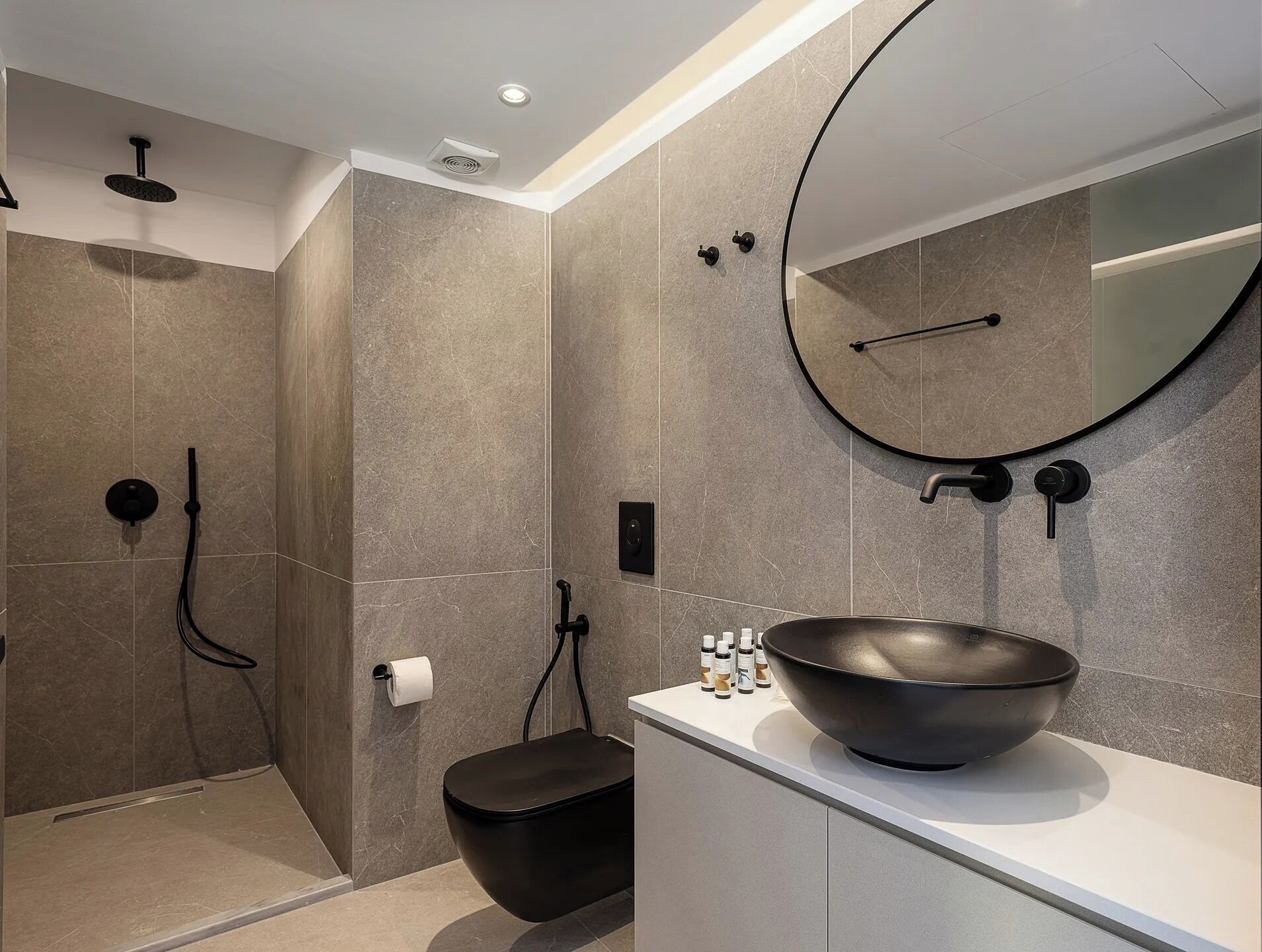Une salle de bain moderne avec un grand miroir rond, un lavabo noir et un espace douche.